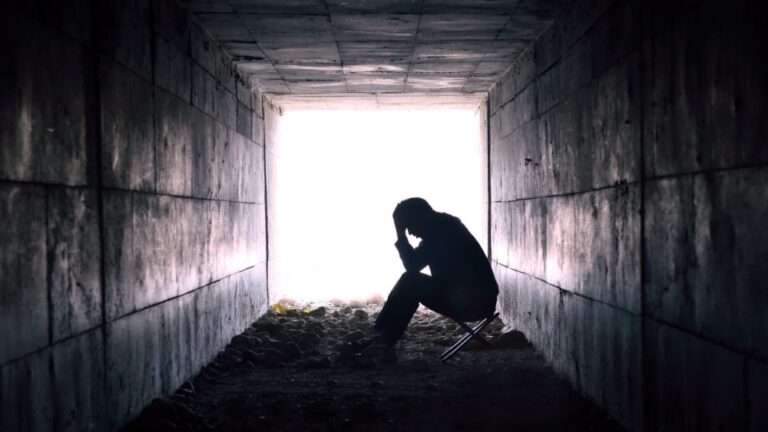 Black and white photograph of person sitting with head in hands in a dark tunnel.