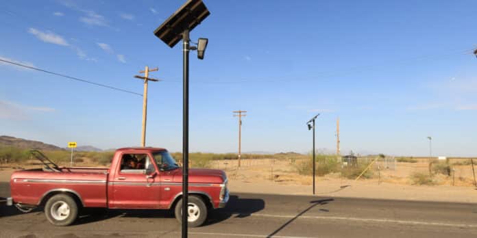 A red truck carrying a lawnmower drives past two Flock Safety automated license plate readers.