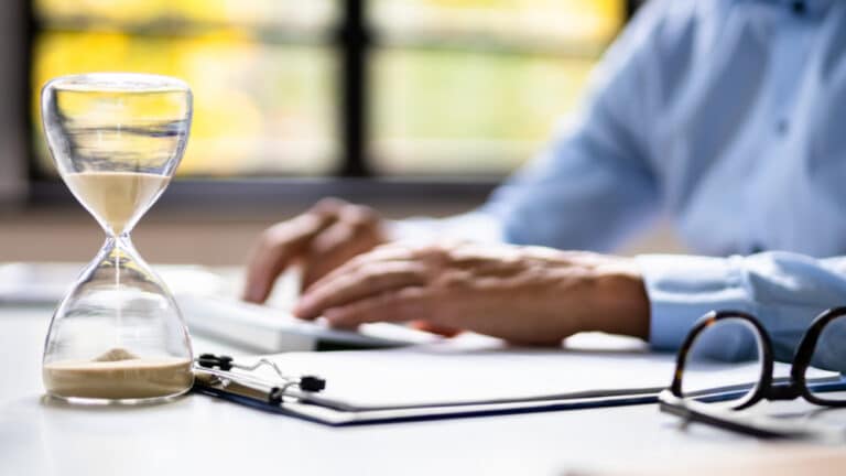 person typing on keyboard with glasses and hourglass next to it