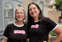 Guía de Regalos de Vacaciones de EFF: Sugerencias para Entusiastas de la Tecnología Two people outside wearing black t-shirts with white trim that say "Let's sue the Government!"