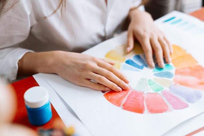 Ciencia y Arte: La Estrategia Visual en la Creación Manos organizando un círculo cromático vibrante sobre papel, ilustrando la base de la teoría del color y la organización de los tonos.