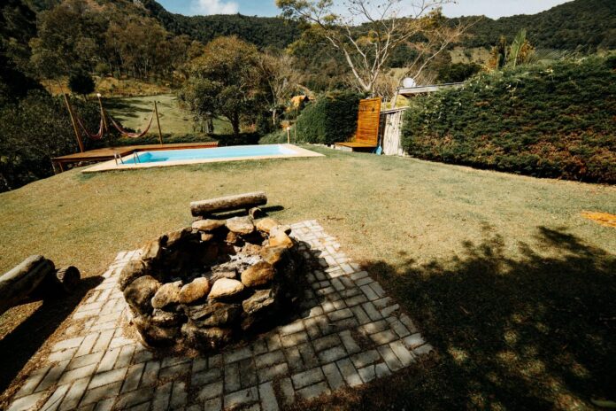 El Arte de Integrar una Piscina de Fibra con un Vista de un jardín con una piscina rectangular y un fogón de piedra rústica, ilustrando la zonificación entre el área de agua y la de fuego.